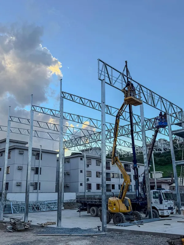 Montagem da estrutura metálica com pilares e treliças, com plataformas elevatórias e caminhão guindaste no canteiro