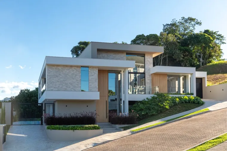 Casa JG vista pelo outro lado da rua, com portão, jardim de entrada e volume em balanço